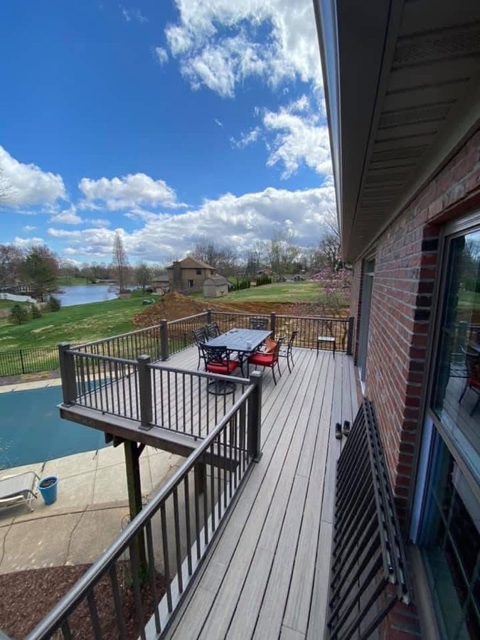 The same deck completed with composite decking, black railing, furniture, and a lake view