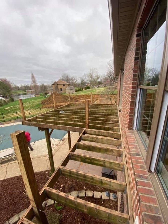 Deck framing under construction above a covered pool, with joists installed and no decking boards yet