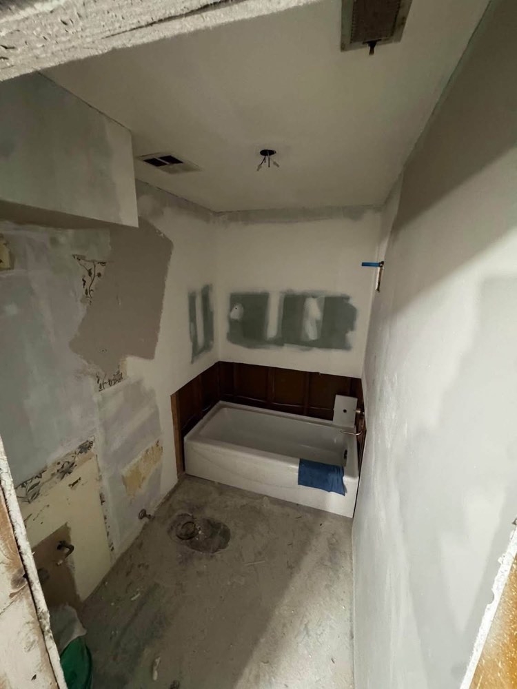 Interior bathroom remodel in progress with drywall patching and a newly set tub