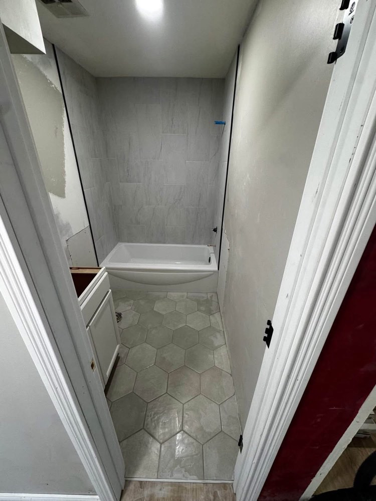 Bathroom remodel progress showing new hexagon floor tile and tiled tub surround