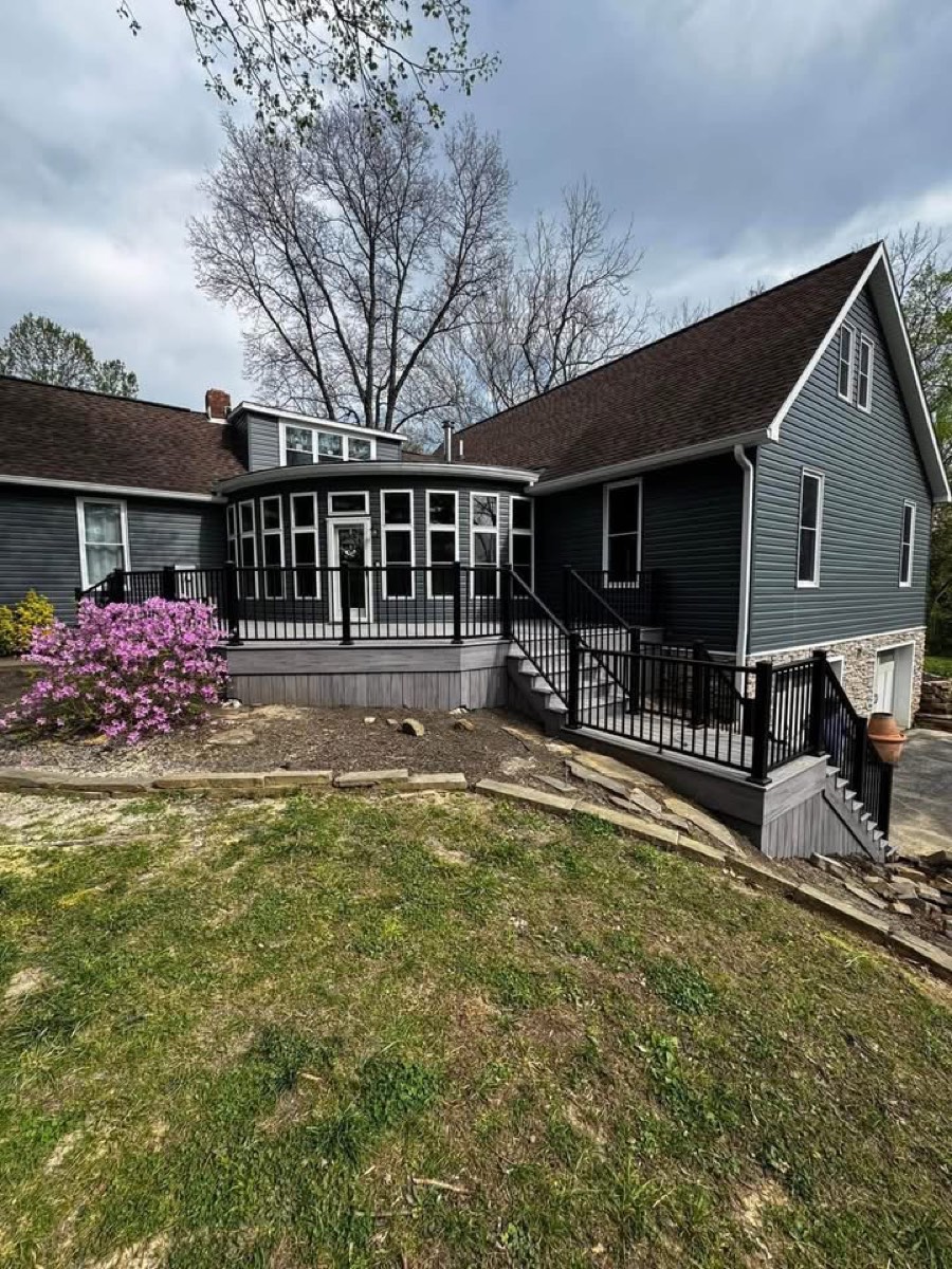 Completed home exterior with new dark siding, composite deck, black railing, and a curved bay window addition
